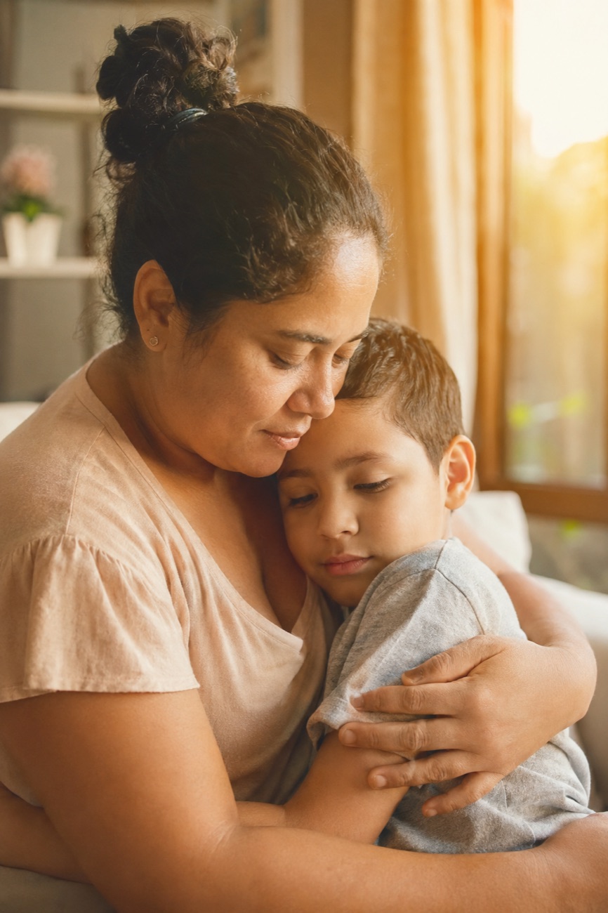 Mãe brasileira abraçando com carinho seu filho criança com autismo, em casa